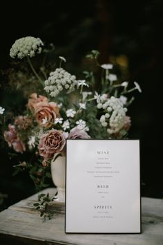 a table with flowers and a menu card on it, sitting next to a vase filled with wildflowers