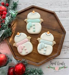 three decorated snowman cookies sitting on top of a wooden tray next to christmas decorations