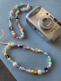 a camera and some beads are laying on the table next to a necklace with smiley faces