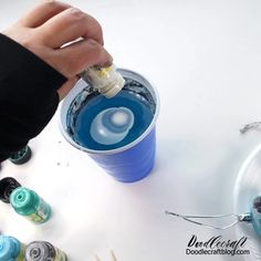 someone is pouring something into a cup with blue liquid in it and other crafting supplies around