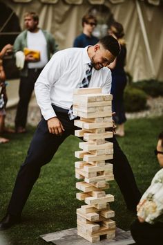 a man in a suit and tie leaning over a tower made out of wooden blocks