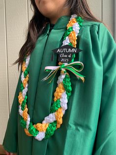 a woman wearing a green graduation gown with a white and yellow ribbon around her neck