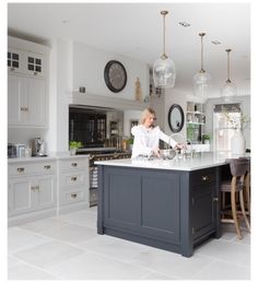 a woman is standing at the center island in a large kitchen with white cabinets and gray countertops