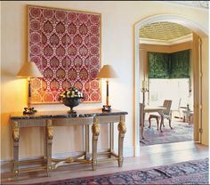 a table with two lamps on top of it in front of a painting and chairs