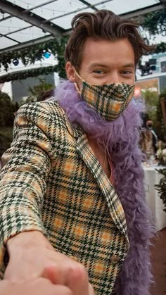 a man wearing a plaid jacket and purple feather around his neck is pointing at the camera