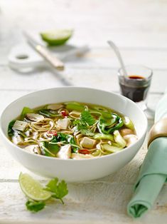 a white bowl filled with noodle soup next to a green napkin and utensils