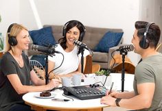 two people sitting at a table with headphones on and one person holding a microphone