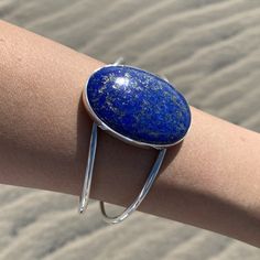 "This beautiful Lapis Lazuli cuff bracelet features a natural untreated large oval crystal cabochon. Features an adjustable sterling silver double band and an open back behind the Lapis Lazuli crystal framework. Beloved Lapis Lazuli is an excellent crystal to wear to enhance the flow of energy through your crown chakra and to enhance your third eye intuitive abilities. Wear this statement bracelet when you need a crystal boost and want to bring out your inner super hero. Dimensions: Crystal: 1.6 Blue Cuff Bracelet Gift, Adjustable Blue Cuff Bangle, Adjustable Silver Bracelet, Third Eye Chakra Stones, Festival Bracelets, Empath Protection, Crystal Centerpieces, Lapis Stone, Lapis Lazuli Crystal