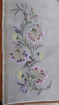 an embroidered piece of cloth with flowers and leaves on the front, sitting on a wooden table