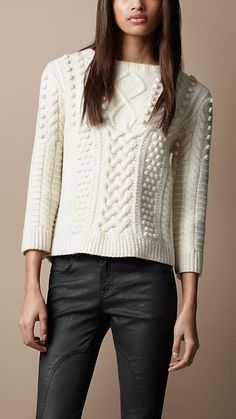 a woman wearing black leather pants and a white cable knit sweater is posing for the camera