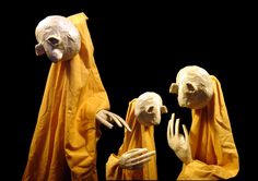 three mannequins dressed in yellow robes and holding hands up to their faces