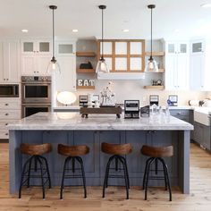 a kitchen with three stools in front of an island and stainless steel appliances on the wall