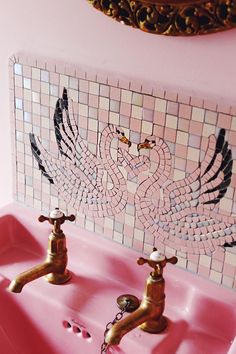 two faucets in a pink sink with mosaic tiles on the wall behind them