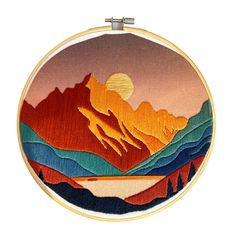 an embroidery project with mountains and the sun in the distance, on a white background