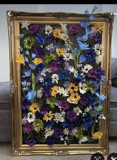 an ornate frame with flowers on it in front of a gray couch and black wall