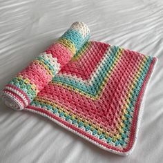 a crocheted blanket laying on top of a bed next to a white pillow