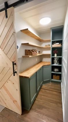 an open door leading to a kitchen with green cabinets and wooden shelves on the wall