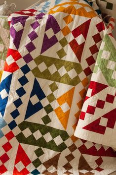 a multicolored quilt sitting on top of a bed next to a white pillow