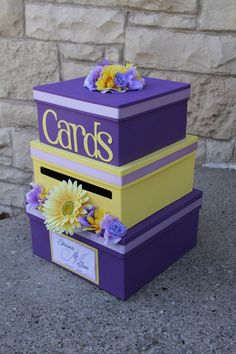 a purple and yellow card box with flowers on the top sitting in front of a brick wall