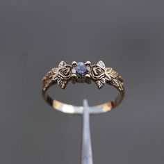 a gold ring with two flowers and a stone in the middle on a metal stand