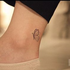 a small butterfly tattoo on the side of a woman's ankle, with black ink