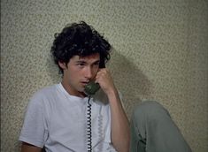 a young man sitting on the floor talking on an old fashioned telephone while holding his hand up to his ear