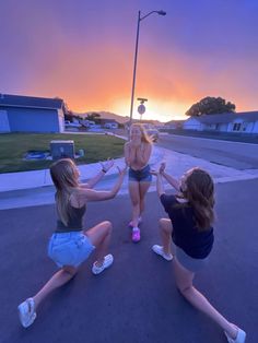 three young women are dancing in the street at sunset