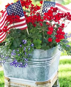 red, white and blue flowers in an old metal bucket with american flags on it