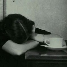 a woman sitting at a table in front of a cup and saucer with her head on her hands