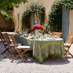 the table is set for two outside with flowers in vases and plates on it