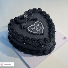 a heart shaped black cake on top of a white table with a note attached to it