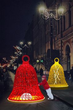 two bell shaped lights on the side of a street at night with people walking by