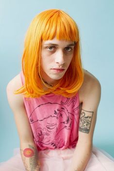 a woman with orange hair and tattoos on her arm sitting in front of a blue background