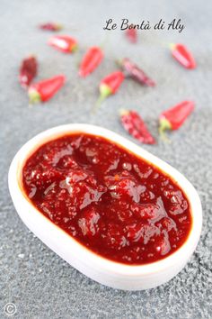 a white bowl filled with red sauce on top of a gray surface next to flowers