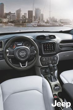 the interior of a vehicle with steering wheel and dashboard controls in front of a cityscape