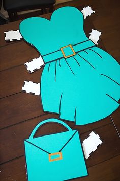 paper cut out of the shape of a woman's dress and purse sitting on top of a wooden floor