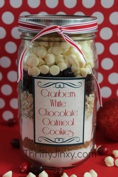 a jar filled with white chocolate covered cookies on top of a red table next to a christmas ornament