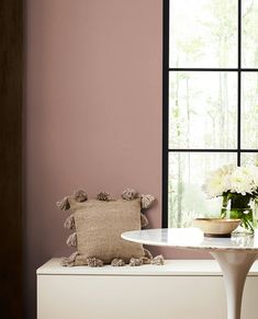 a vase with flowers sitting on top of a white table next to a large window