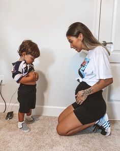 a woman kneeling down next to a little boy with tattoos on his arms and legs