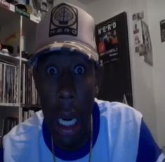 a man wearing a hat with his mouth wide open in front of a shelf full of cds