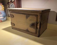 an old wooden box sitting on top of a counter next to a clock and figurine