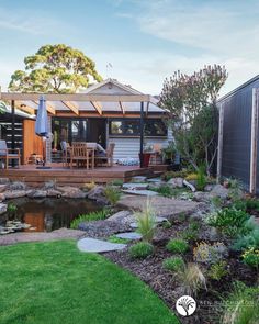 a backyard with a small pond and decking in the middle, surrounded by greenery