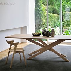 a wooden table sitting in front of a window next to a vase on top of a rug