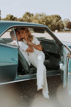 a man and woman sitting in the back of a blue car, kissing each other