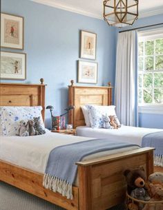 two beds in a room with blue walls and pictures on the wall above them, one has a teddy bear