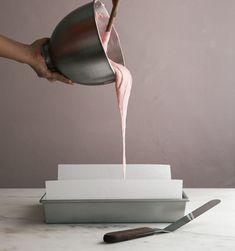 a person pours pink liquid into a cup from a saucepan on a counter