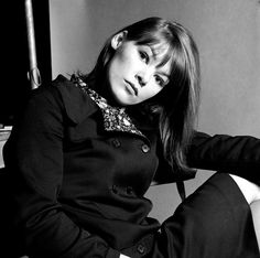 black and white photograph of a woman sitting on a chair with her legs crossed, looking at the camera