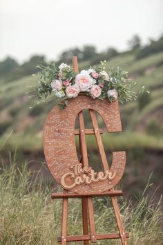 a wooden easel decorated with flowers and the word love is displayed in front of a grassy hill