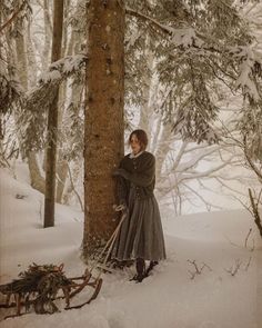 a woman standing next to a tree in the snow