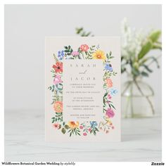 a wedding card with colorful flowers and greenery on the front, sitting next to a vase